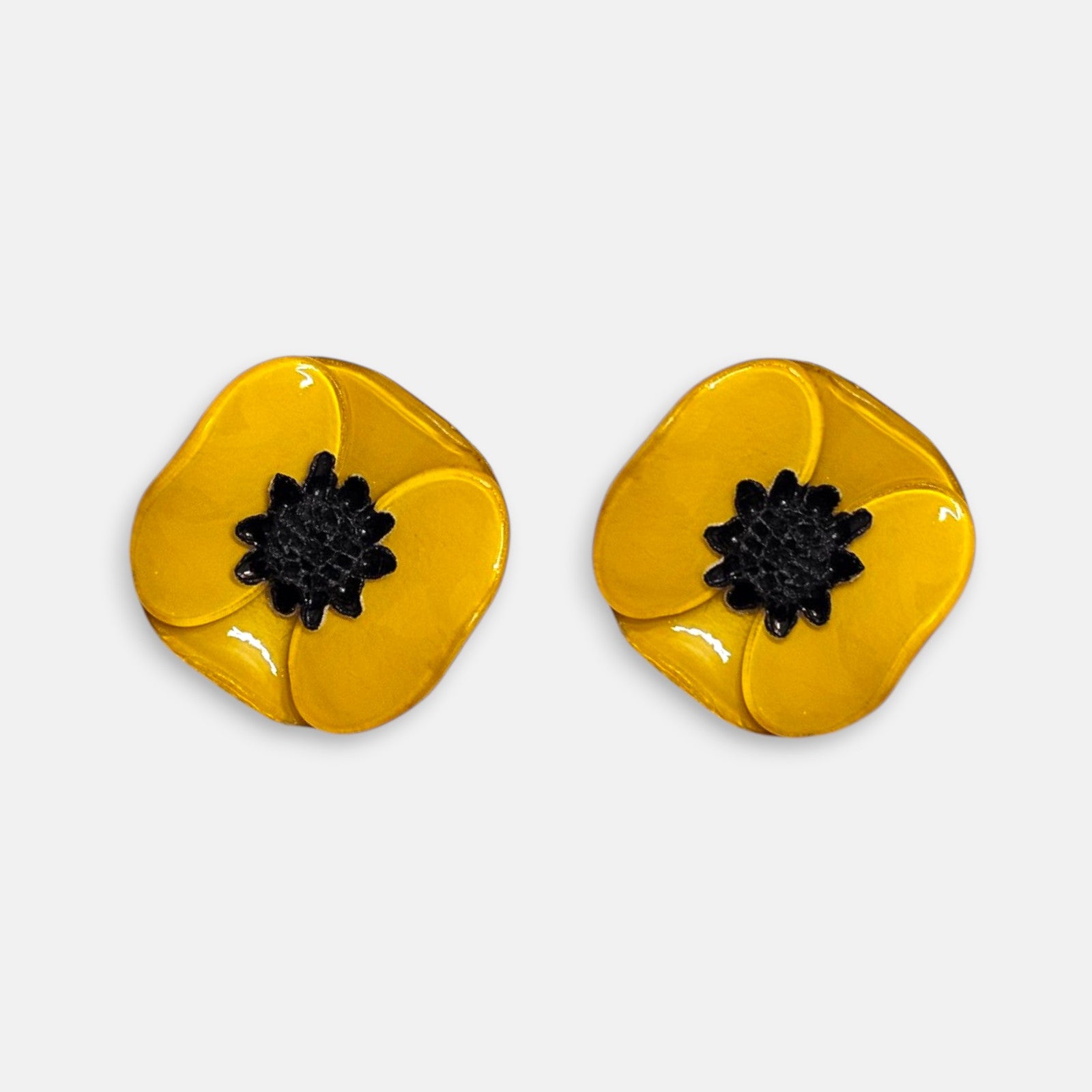 par de pendientes pequeños de clip con forma de flor de amapola de Ciléa Paris, detallando sus pétalos de resina esmaltada en tono amarillo ocre y su centro negro estrellado.