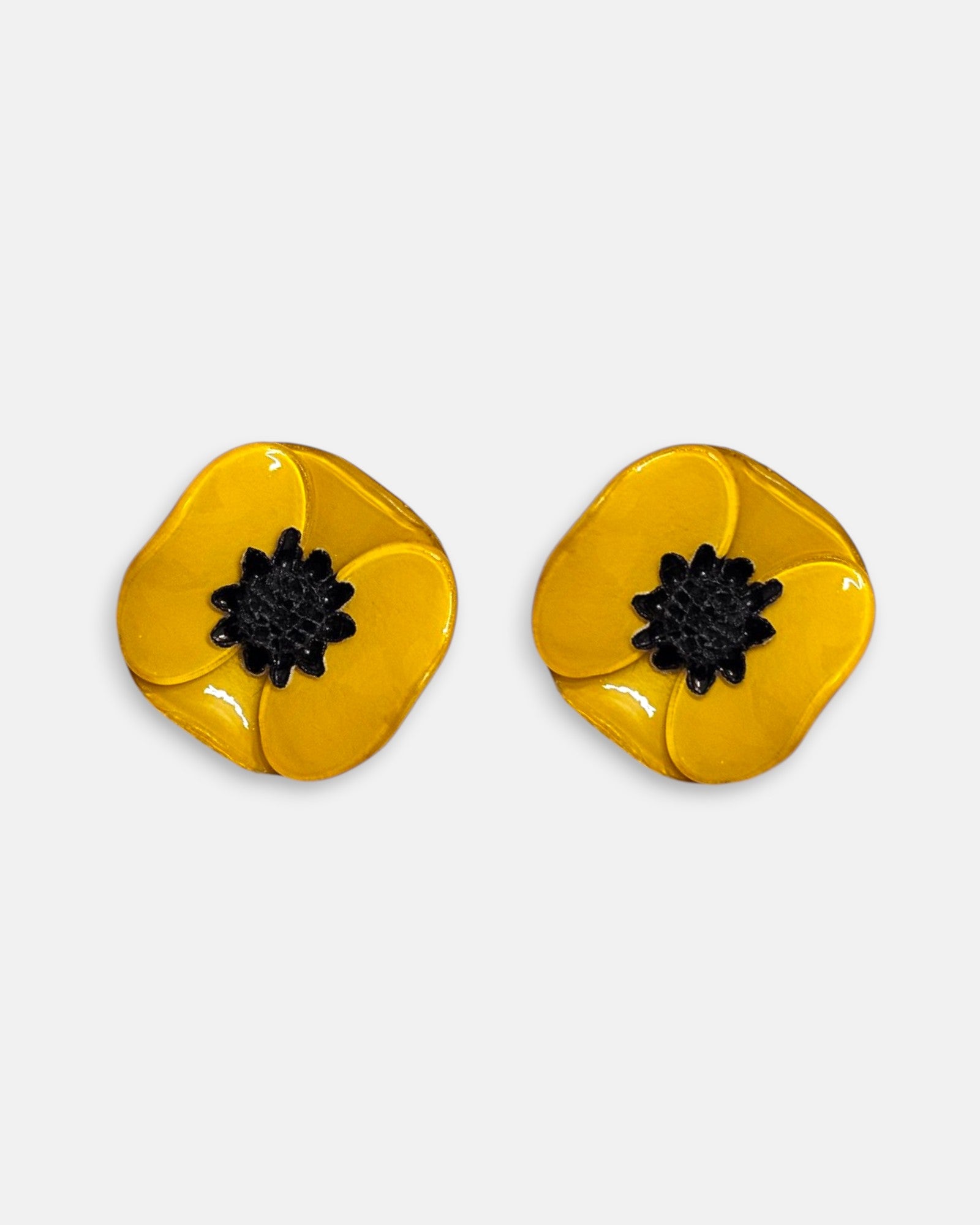 par de pendientes pequeños de clip con forma de flor de amapola de Ciléa Paris, detallando sus pétalos de resina esmaltada en tono amarillo ocre y su centro negro estrellado.