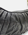 primer plano macro de la textura de la piel negra del bolso Carlotta, permitiendo apreciar los pliegues verticales y el fino graneado del material.