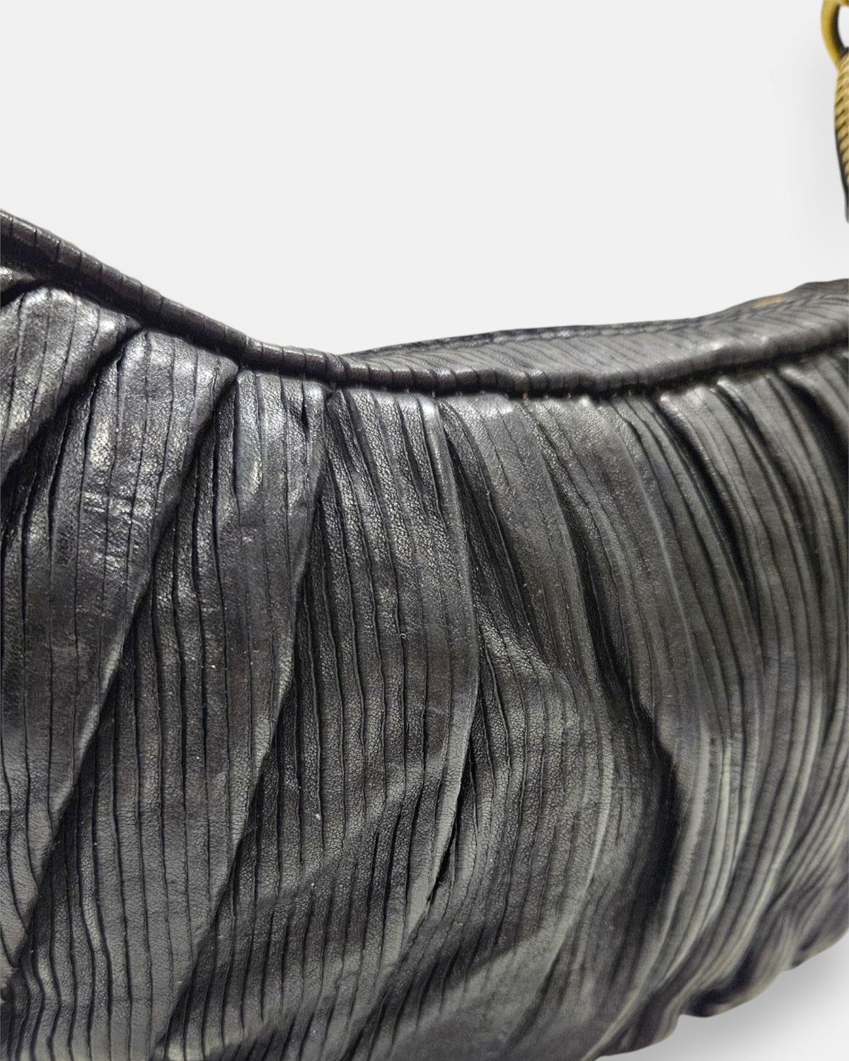 primer plano macro de la textura de la piel negra del bolso Carlotta, permitiendo apreciar los pliegues verticales y el fino graneado del material.