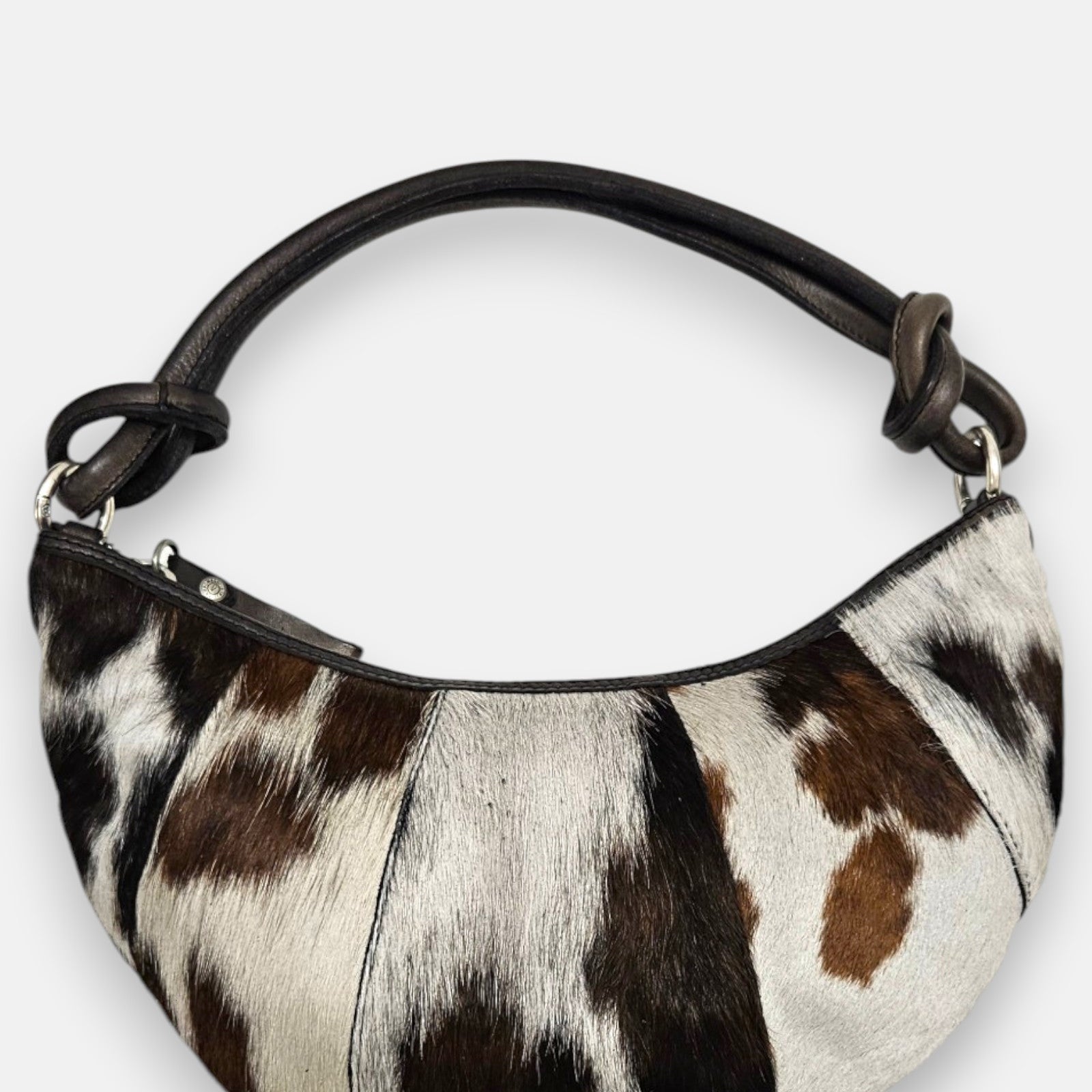 bolso Gaia de piel con pelo corto manchado en tonos blanco, marrón y negro, silueta media luna y asa anudada.