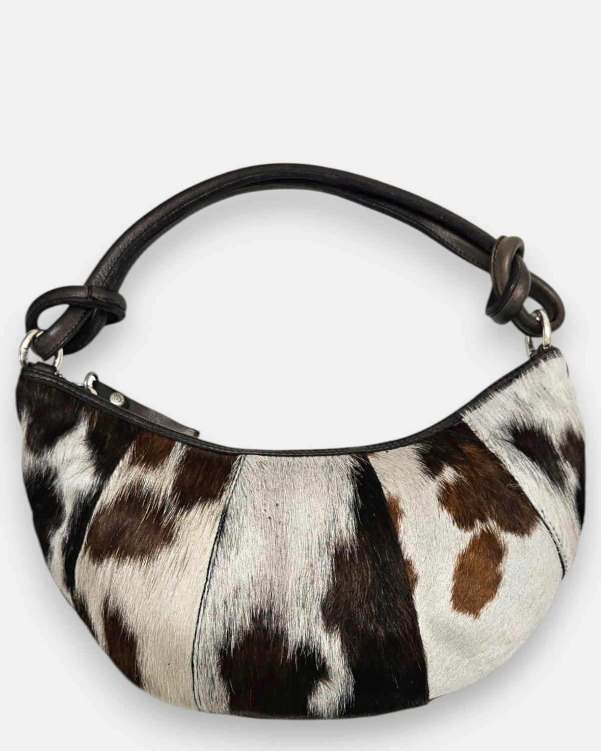 bolso Gaia de piel con pelo corto manchado en tonos blanco, marrón y negro, silueta media luna y asa anudada.