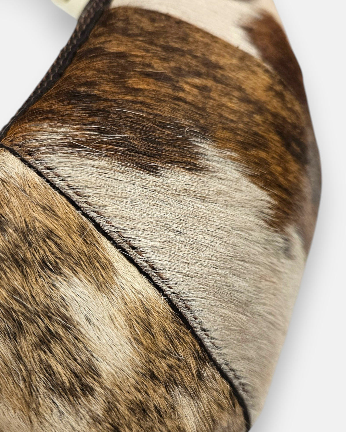 primer plano macro de la textura frontal del bolso Elena, permitiendo apreciar el brillo del pelo corto, las vetas naturales y el minucioso pespunte de la costura.