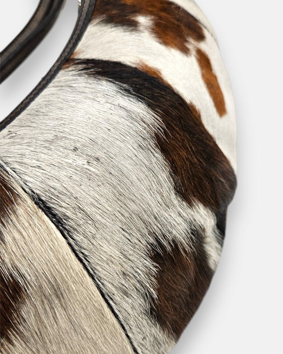 primer plano macro de la textura frontal del bolso Gaia, permitiendo apreciar el brillo del pelo corto, las vetas naturales y el minucioso pespunte de la costura.
