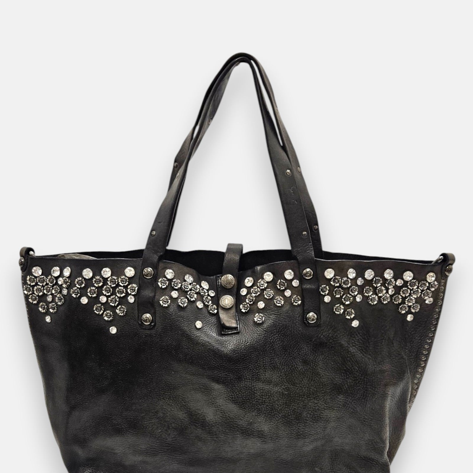 bolso Chiara de piel gris, destacando su franja superior ornamentada con cristales y apliques florales metálicos junto a sus asas dobles.