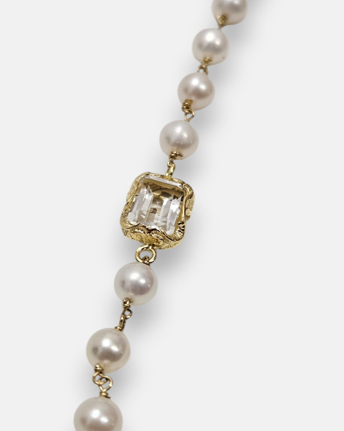 primer plano macro de la pulsera Fiorenza, permitiendo apreciar el cincelado artesanal del engaste chapado en oro, la transparencia del cristal esmeralda y la perla nacarada.
