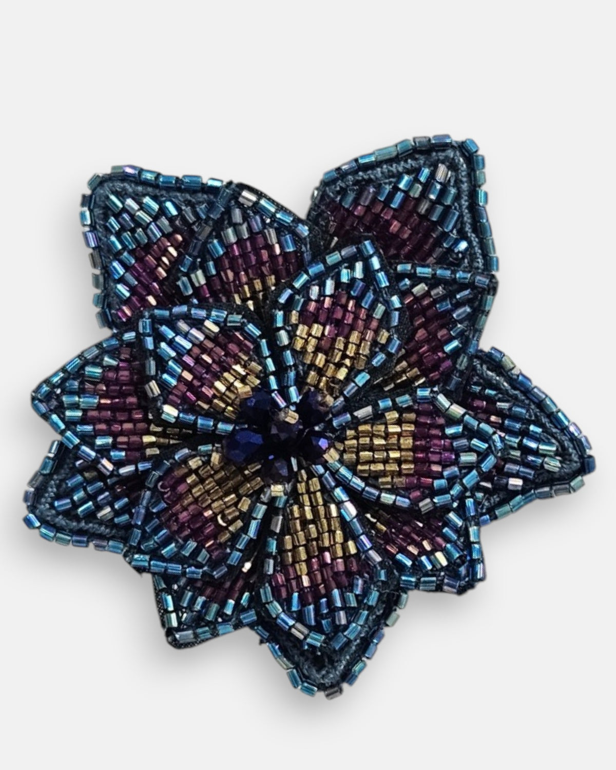 primer plano macro del pendiente Fleur de Lotus Multicolore, permitiendo apreciar el trabajo artesanal de las microcuentas en azul, púrpura y oro con los destellos iridiscentes del centro.