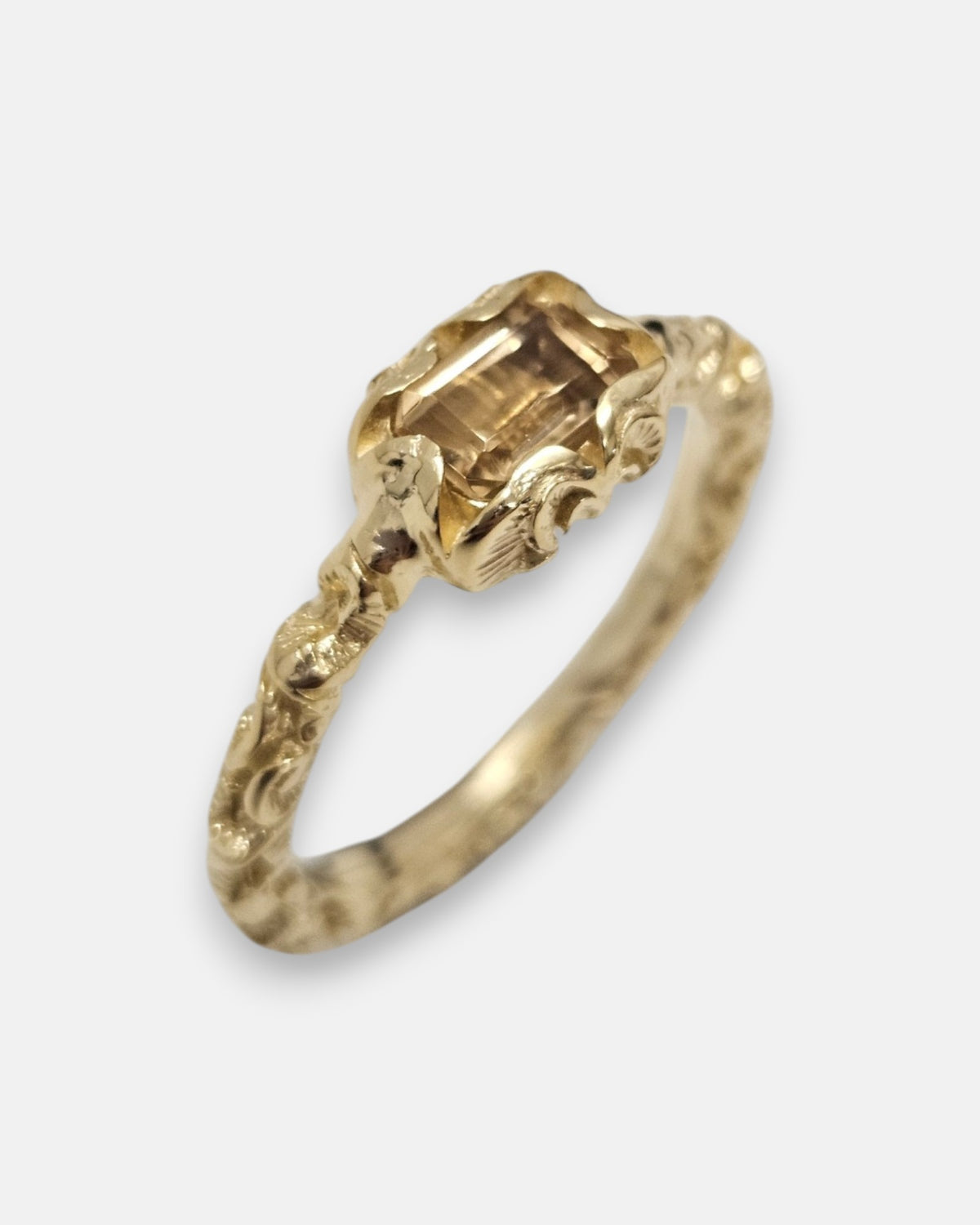 primer plano macro del anillo Nereo, permitiendo apreciar el cincelado artesanal del cáliz chapado en oro y las facetas rectangulares del cristal ámbar.