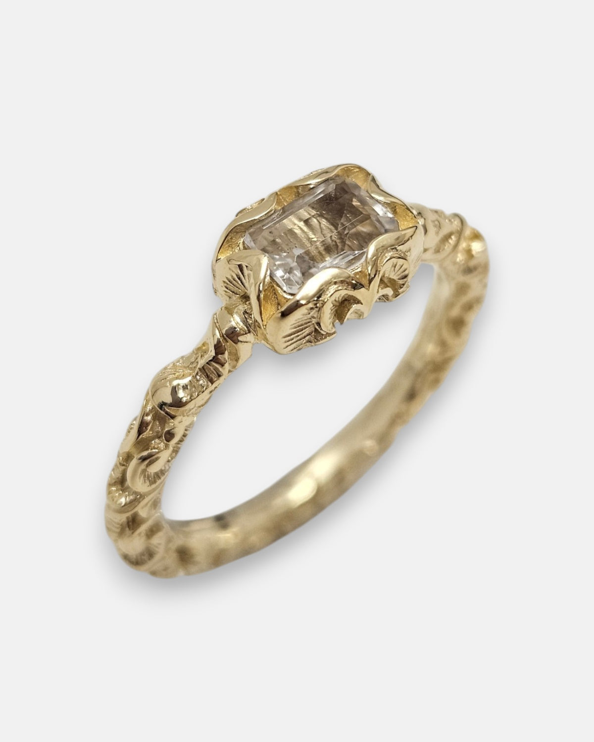 primer plano macro del anillo Zeno, permitiendo apreciar el cincelado artesanal del cáliz chapado en oro y las facetas rectangulares del cristal transparente.