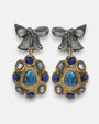 pendientes Colette Bleu de Dominique Denaive en resina artesanal con lazo gris y medallón dorado con cabujones azules.