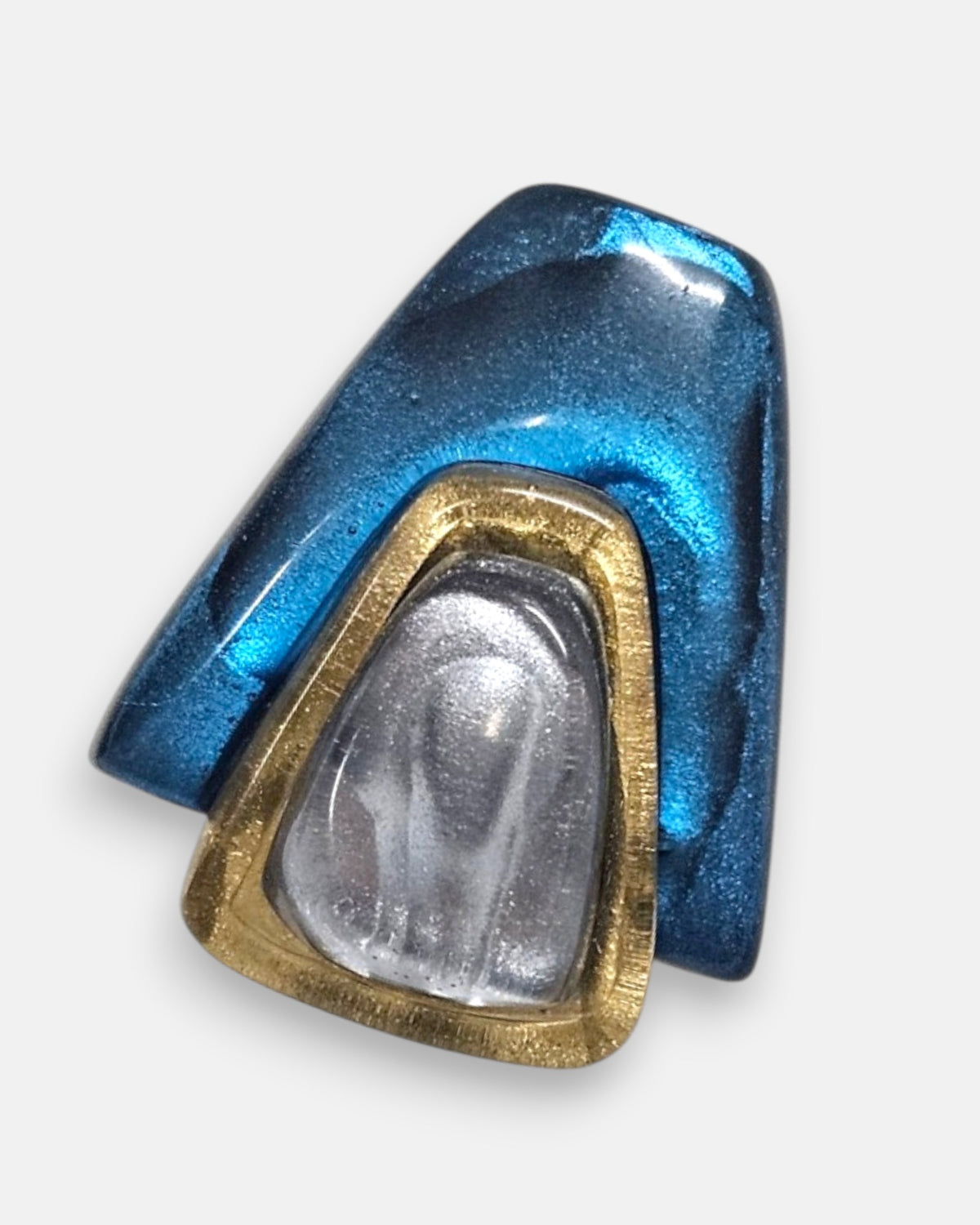 primer plano macro del pendiente Solène Azur, permitiendo apreciar el pulido artesanal y los destellos metalizados de la resina azul y gris.