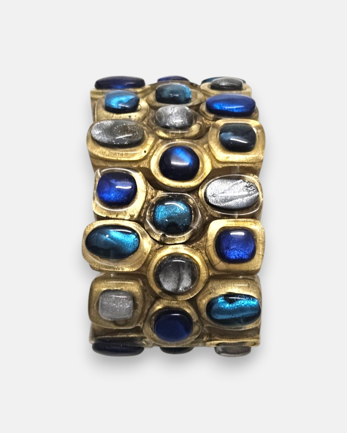 primer plano macro de la pulsera Océane Bleu, permitiendo apreciar los cabujones iridiscentes en azul cobalto, turquesa y plata nacarada sobre la base dorada.