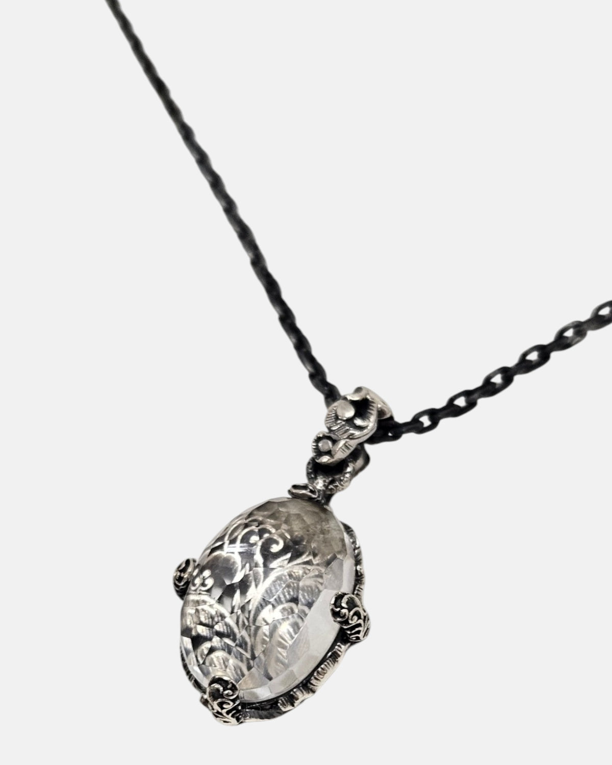 primer plano macro del colgante Médaillon Transparent et Argent Baroque de Maria e Luisa, permitiendo apreciar la talla faceteada del cristal, la reasa ornamentada y las garras de plata envejecida.