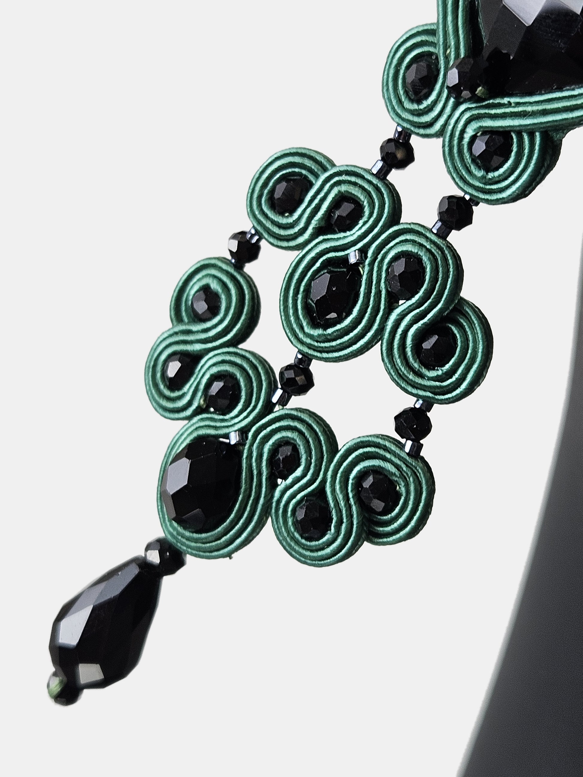 Detalle del complejo trenzado de seda verde esmeralda y el facetado de los cristales negros del pendiente artesanal.