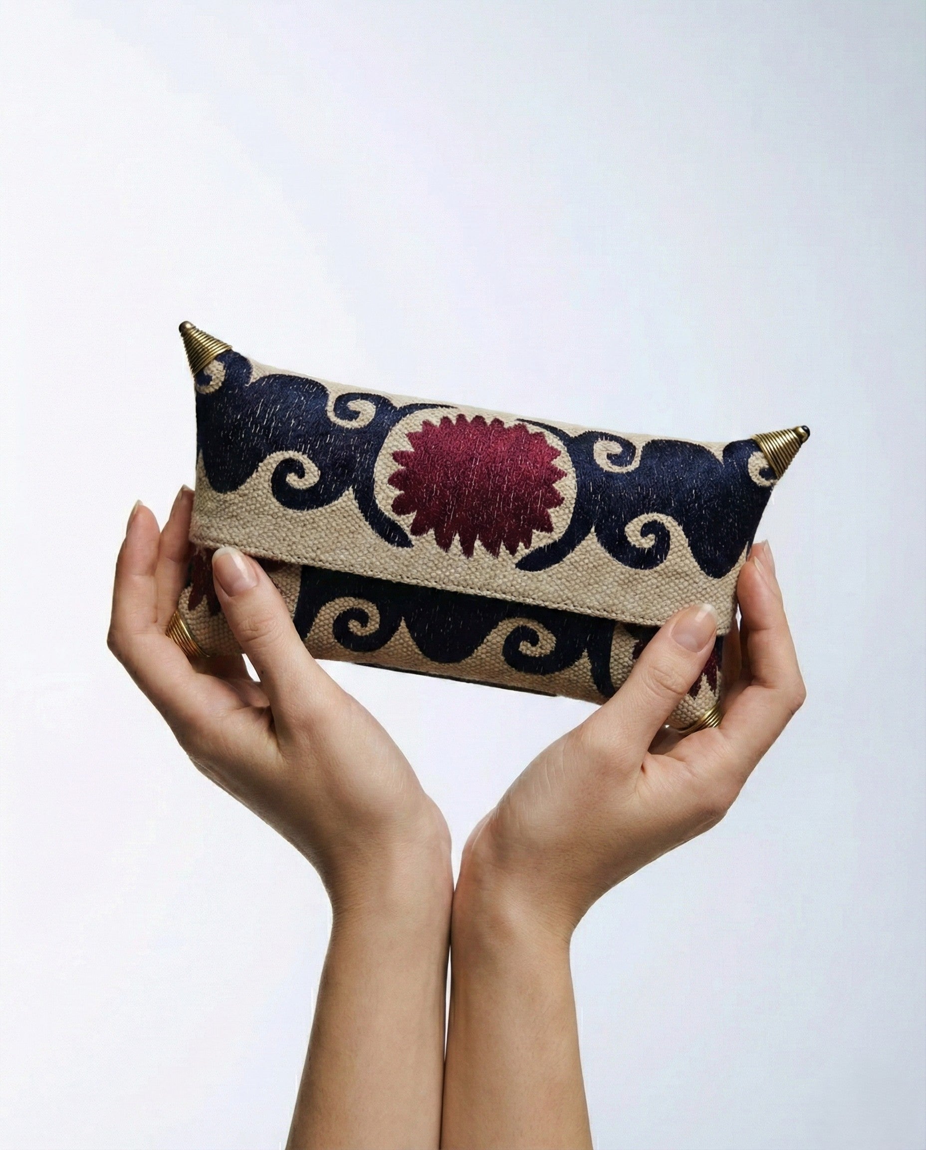 Manos de modelo sosteniendo el clutch bordado en azul y burgundy, resaltando el diseño simétrico y el acabado de lujo de los herrajes laterales.