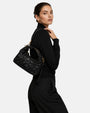 modelo luciendo el bolso trenzado negro colgado al hombro, apreciando su tamaño proporcional, su silueta curva y su elegancia casual.