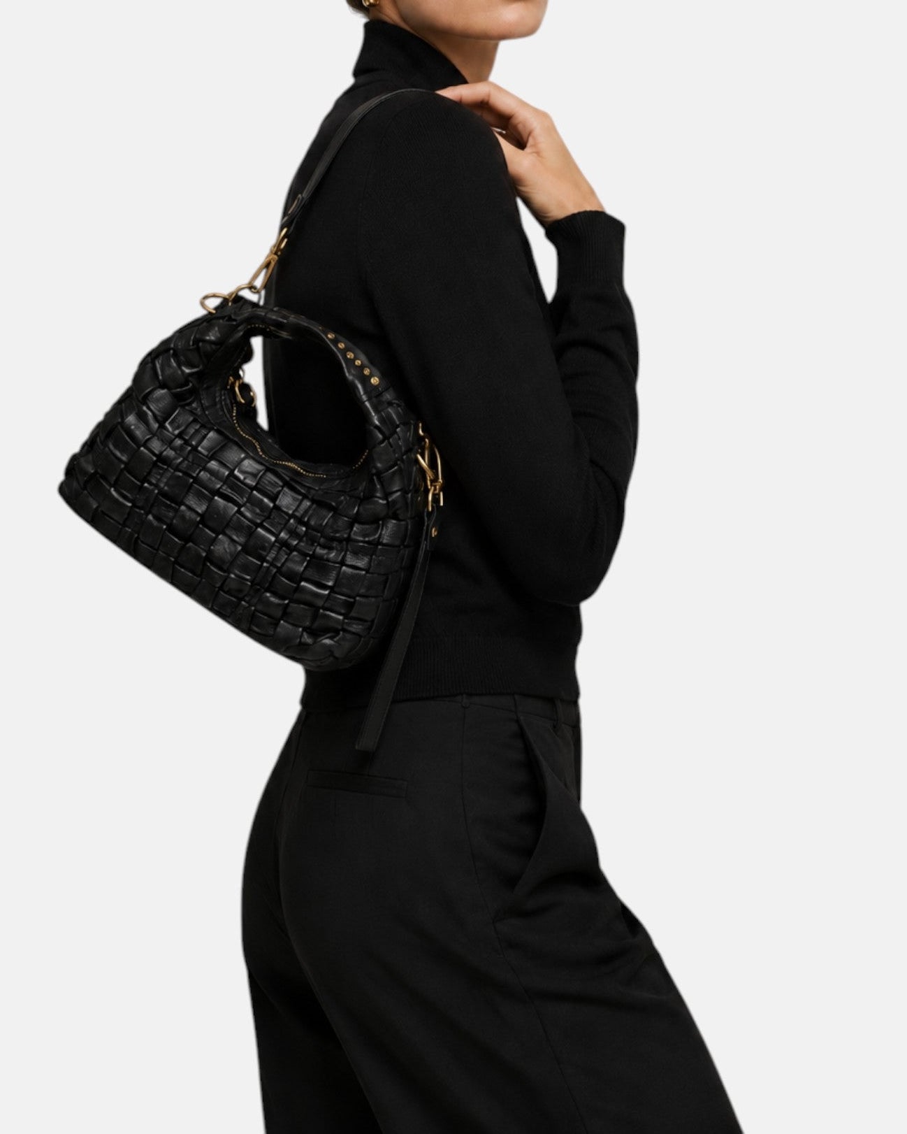 modelo luciendo el bolso trenzado negro colgado al hombro, apreciando su tamaño proporcional, su silueta curva y su elegancia casual.