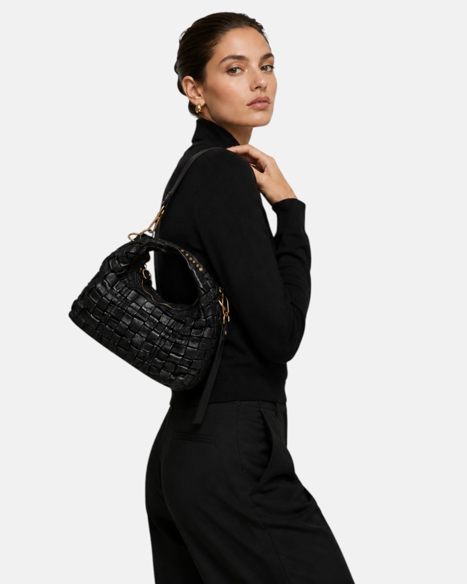modelo luciendo el bolso trenzado negro colgado al hombro, apreciando su tamaño proporcional, su silueta curva y su elegancia casual.