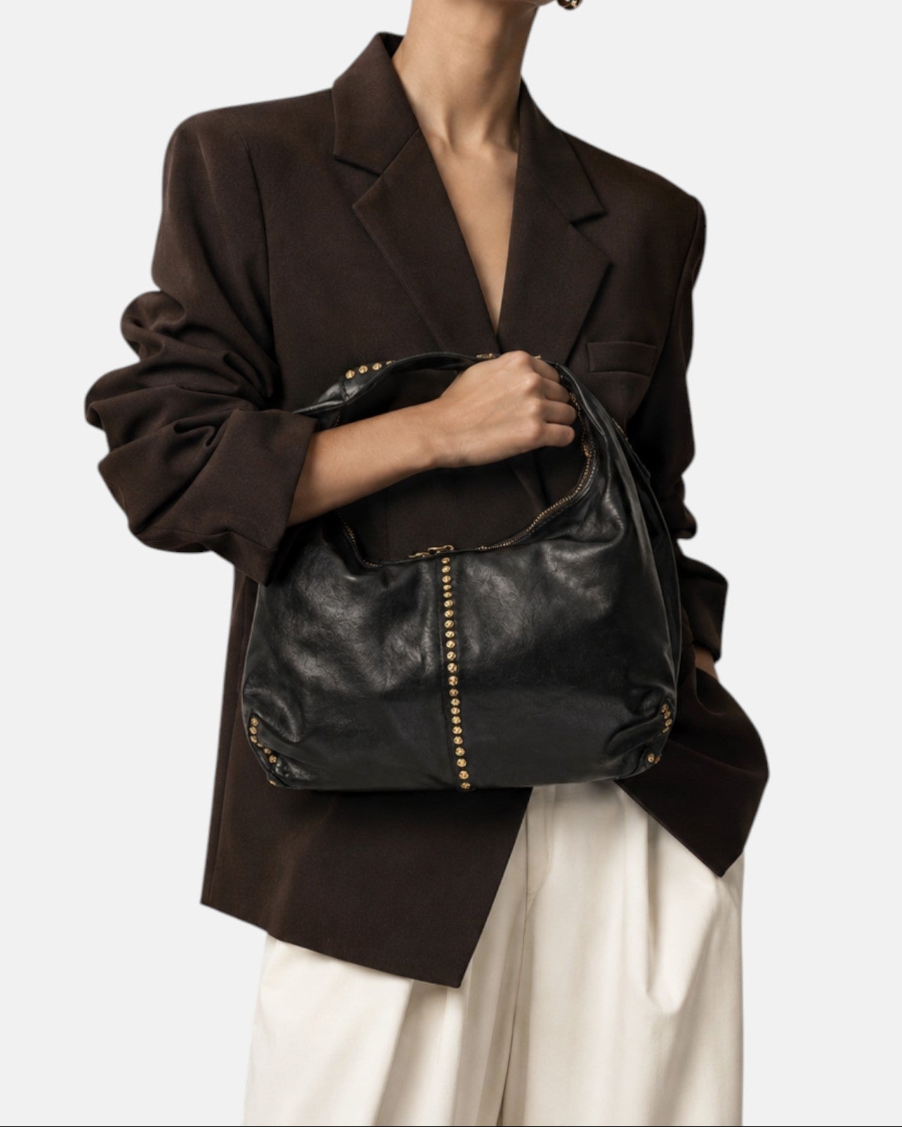modelo sosteniendo en la mano el bolso Francesca sobre una americana oscura, apreciando su silueta curva y su tamaño proporcional.