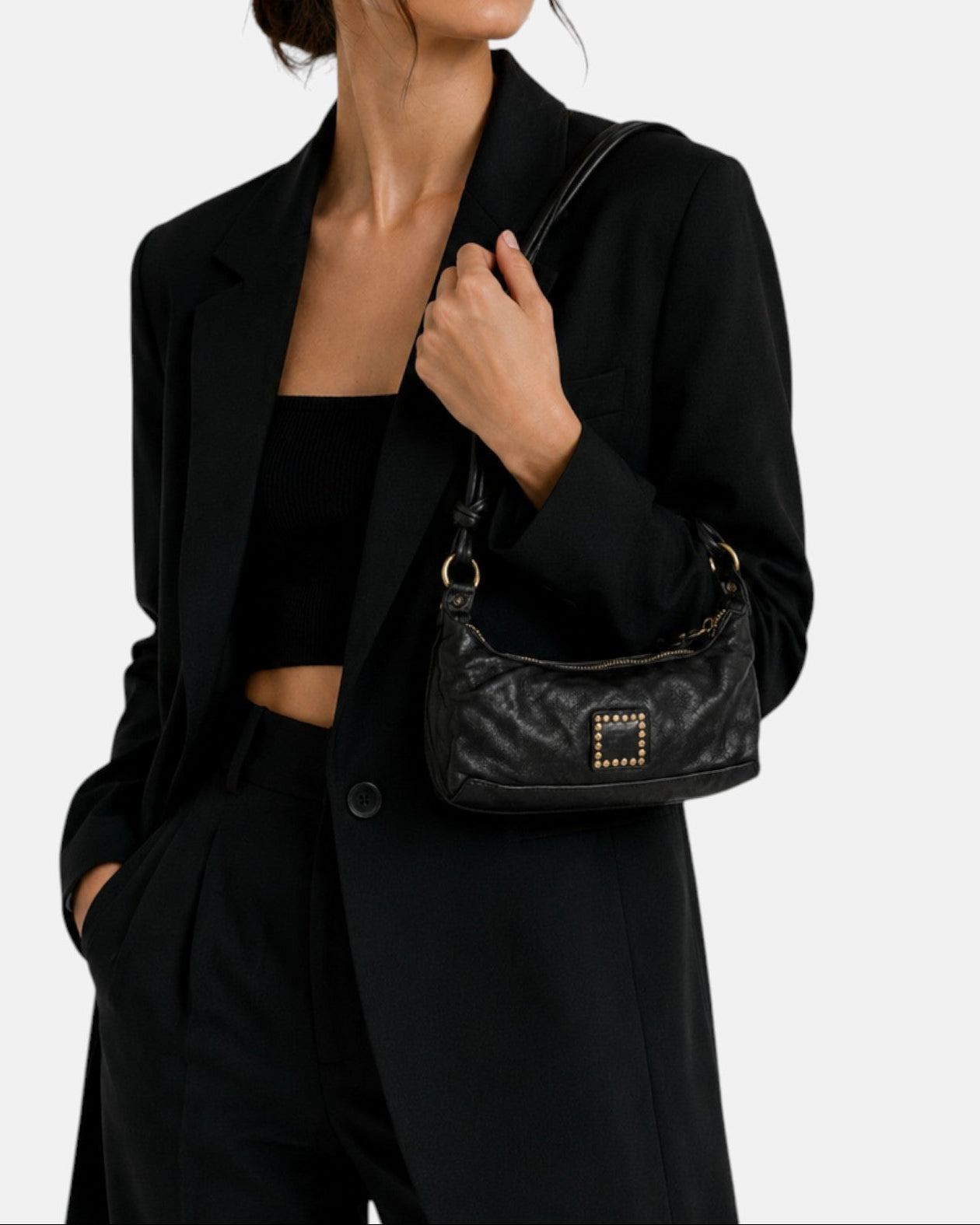 modelo luciendo el bolso Bianca colgado al hombro sobre un traje negro, apreciando su tamaño compacto y su estilo sobrio.