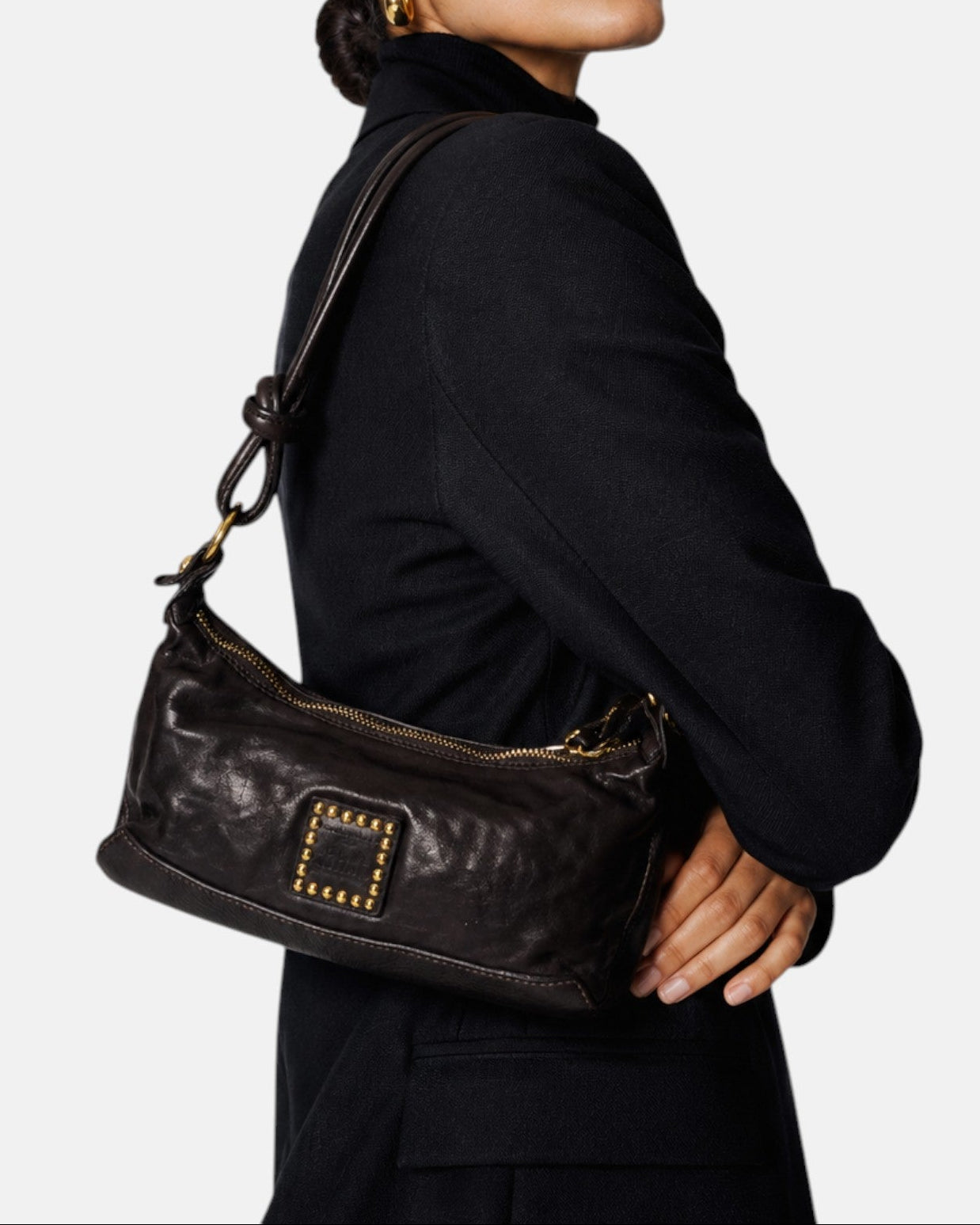 modelo luciendo el bolso Camilla colgado al hombro sobre un traje oscuro, apreciando su tamaño compacto y su estilo sobrio.
