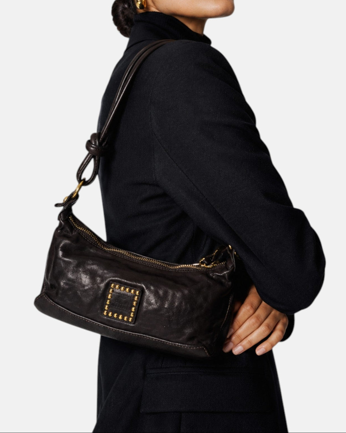 modelo luciendo el bolso Camilla colgado al hombro sobre un traje oscuro, apreciando su tamaño compacto y su estilo sobrio.
