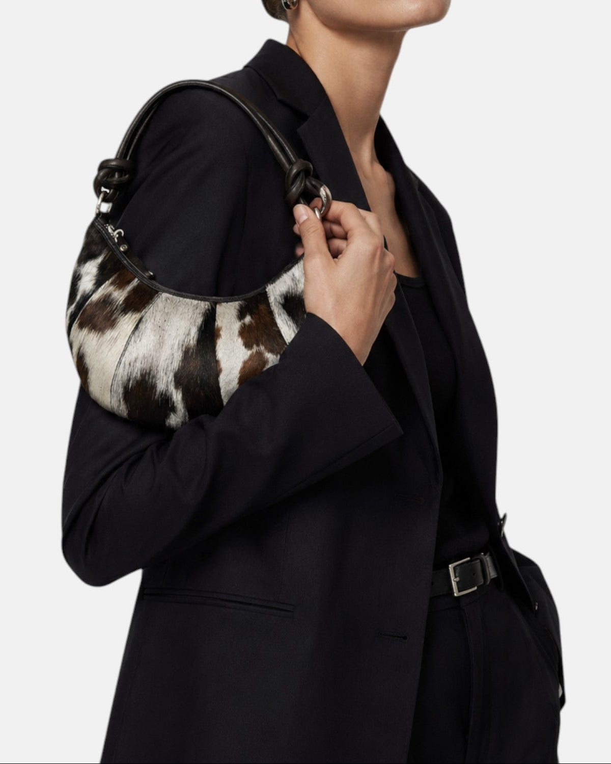 modelo luciendo el bolso Gaia colgado al hombro sobre un traje oscuro, apreciando su escala cómoda y su textura silvestre.