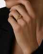 modelo luciendo el anillo Nereo en la mano, apreciando su destello miel y acabado dorado sobre la piel.