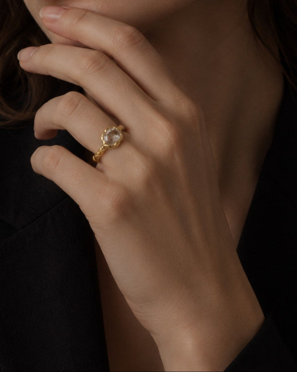 modelo luciendo el anillo Aura en la mano, apreciando su destello delicado y acabado dorado.