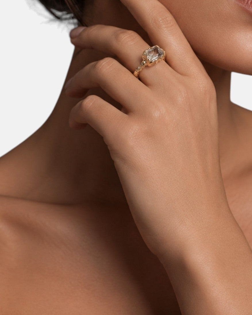 modelo luciendo el anillo Zeno en la mano, apreciando su corte esmeralda y destello dorado sobre la piel.