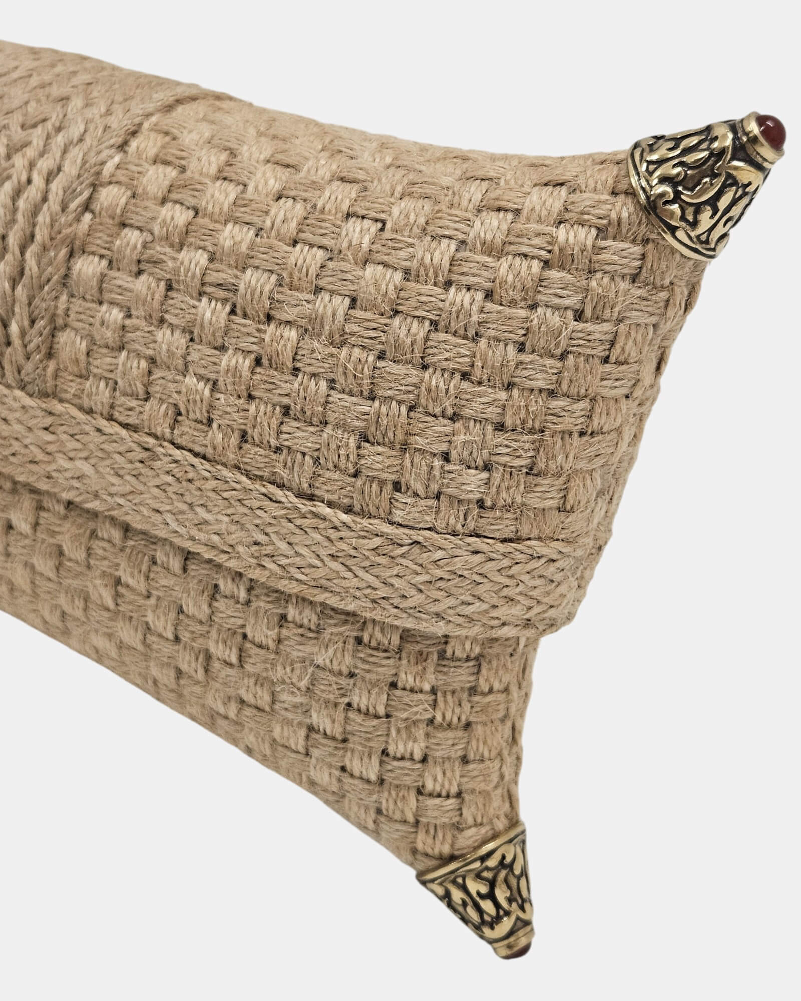 Detalle en primer plano del trenzado de fibra natural y esquinera de metal dorado envejecido con relieve floral y piedra roja, resaltando la calidad artesanal del bolso.