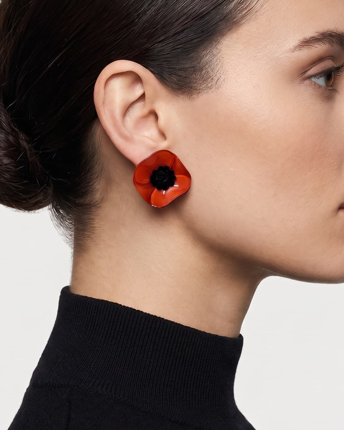 modelo luciendo el pendiente de botón de amapola mini, apreciando su escala delicada y cómo se acopla con elegancia al lóbulo aportando un toque de color rojo muy sofisticado.