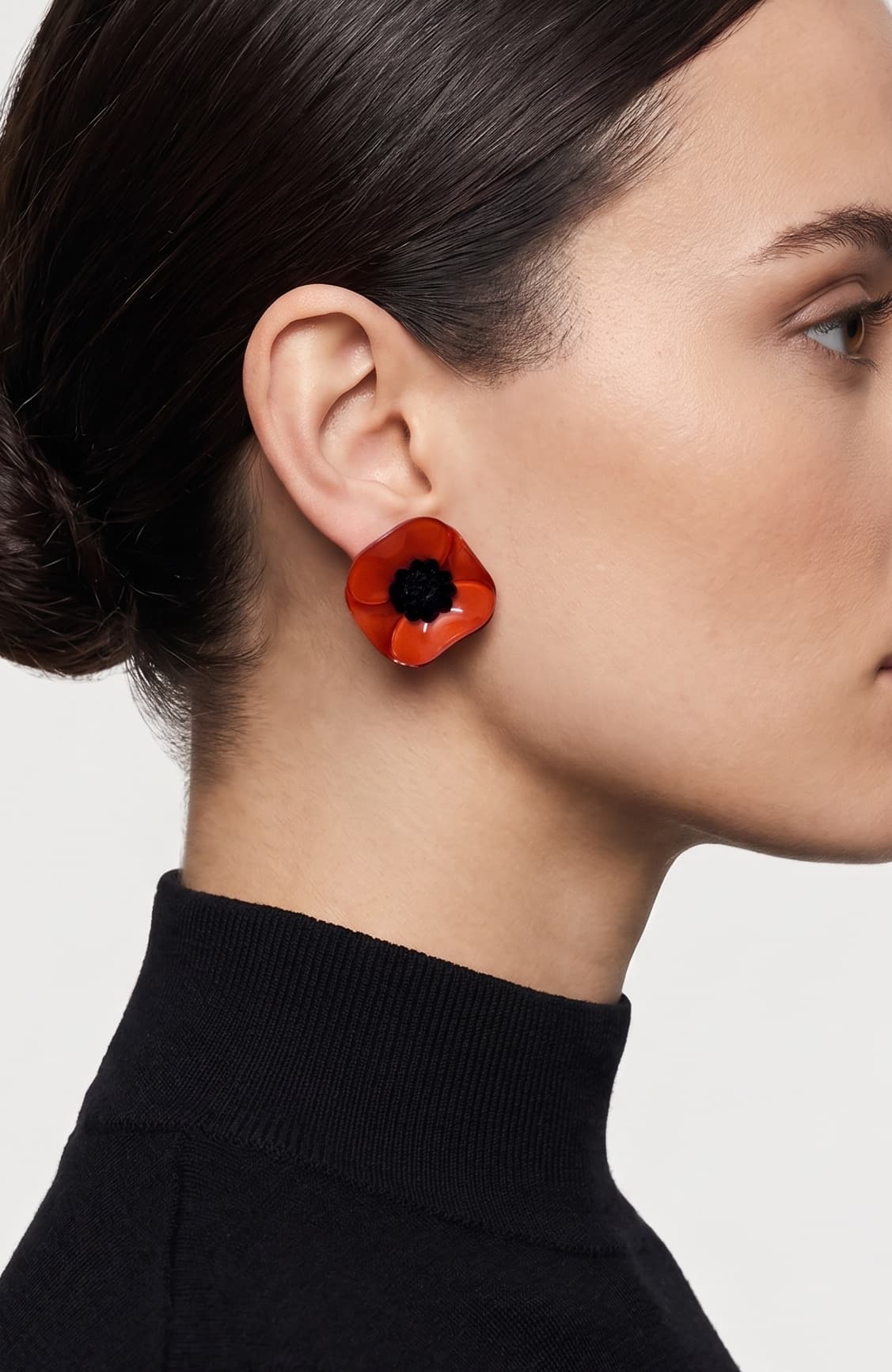 modelo luciendo el pendiente de botón de amapola mini, apreciando su escala delicada y cómo se acopla con elegancia al lóbulo aportando un toque de color rojo muy sofisticado.