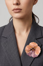 vista frontal de una modelo con el broche de pensamiento pastel de Ciléa Paris prendido de forma elegante en la solapa de una chaqueta gris de sastre, resaltando su formato de 7.5x7.5 cm.