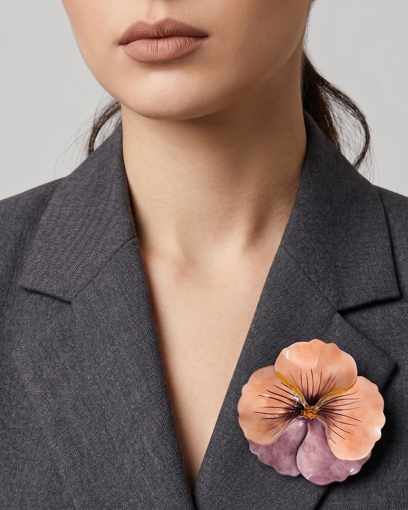 vista frontal de una modelo con el broche de pensamiento pastel de Ciléa Paris prendido de forma elegante en la solapa de una chaqueta gris de sastre, resaltando su formato de 7.5x7.5 cm.