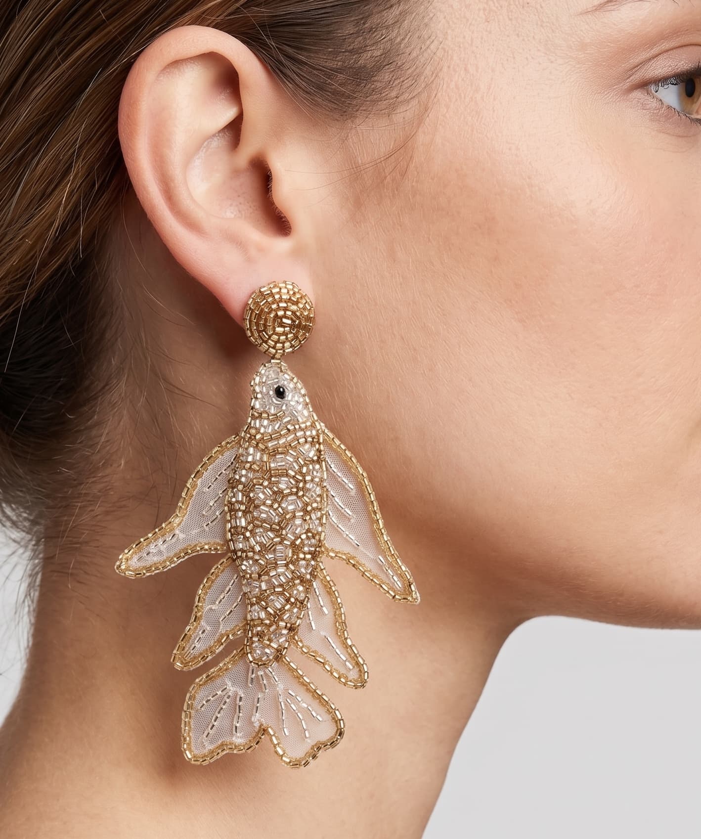 Primer plano lateral de mujer luciendo los pendientes "Danza de Oro", resaltando su diseño vertical, transparencia y brillo metálico.