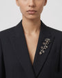 Detalle de una blazer negra con el broche "Rama Silvestre" colocado de forma vertical en la solapa izquierda.