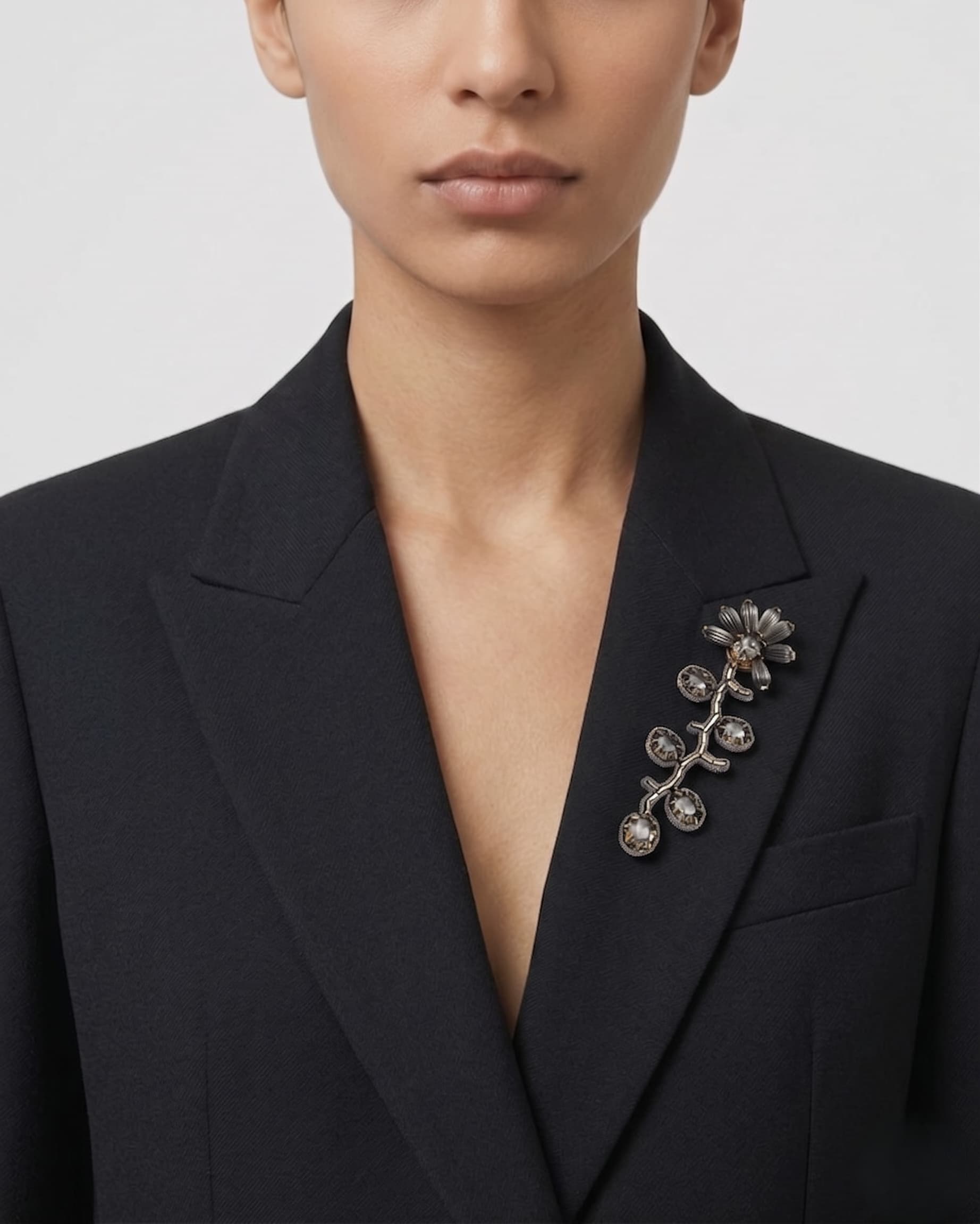 Detalle de una blazer negra con el broche "Rama Silvestre" colocado de forma vertical en la solapa izquierda.