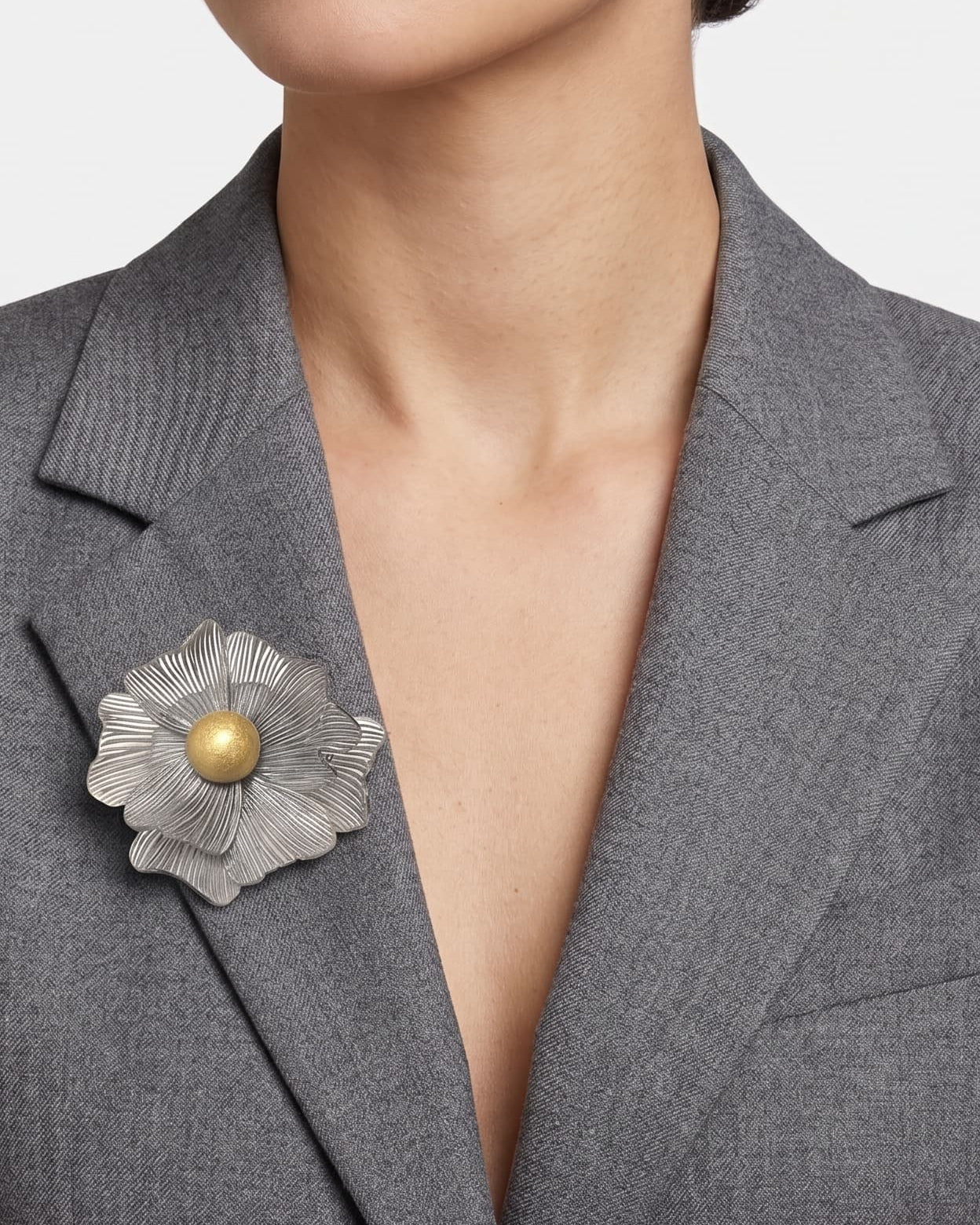 modelo de frente luciendo el broche maxi de anémona plateada prendido en la solapa de una chaqueta de sastre gris, mostrando su escala elegante.