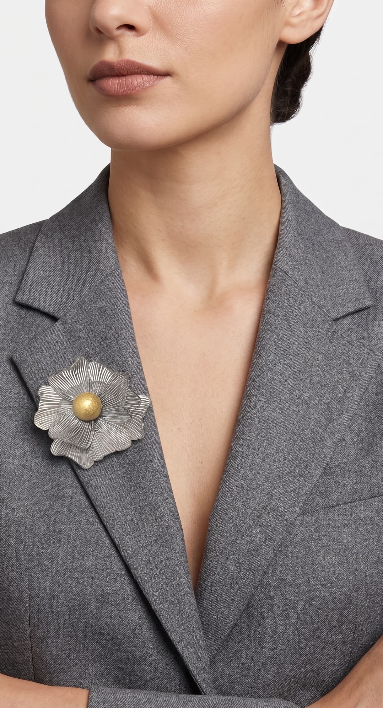 modelo de frente luciendo el broche maxi de anémona plateada prendido en la solapa de una chaqueta de sastre gris, mostrando su escala elegante.