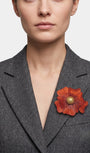 modelo de frente portando el broche maxi de anémona naranja prendido en la solapa de una americana de sastre gris oscuro, apreciando su escala y relieve.