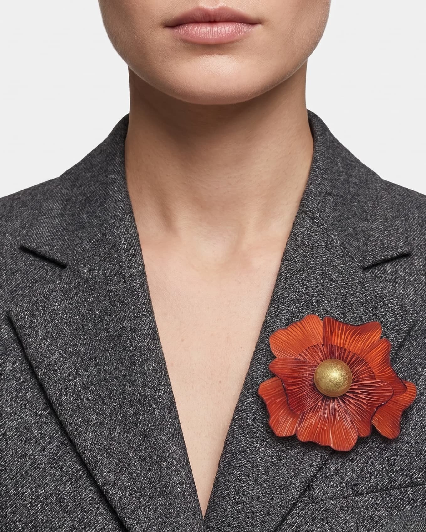modelo de frente portando el broche maxi de anémona naranja prendido en la solapa de una americana de sastre gris oscuro, apreciando su escala y relieve.