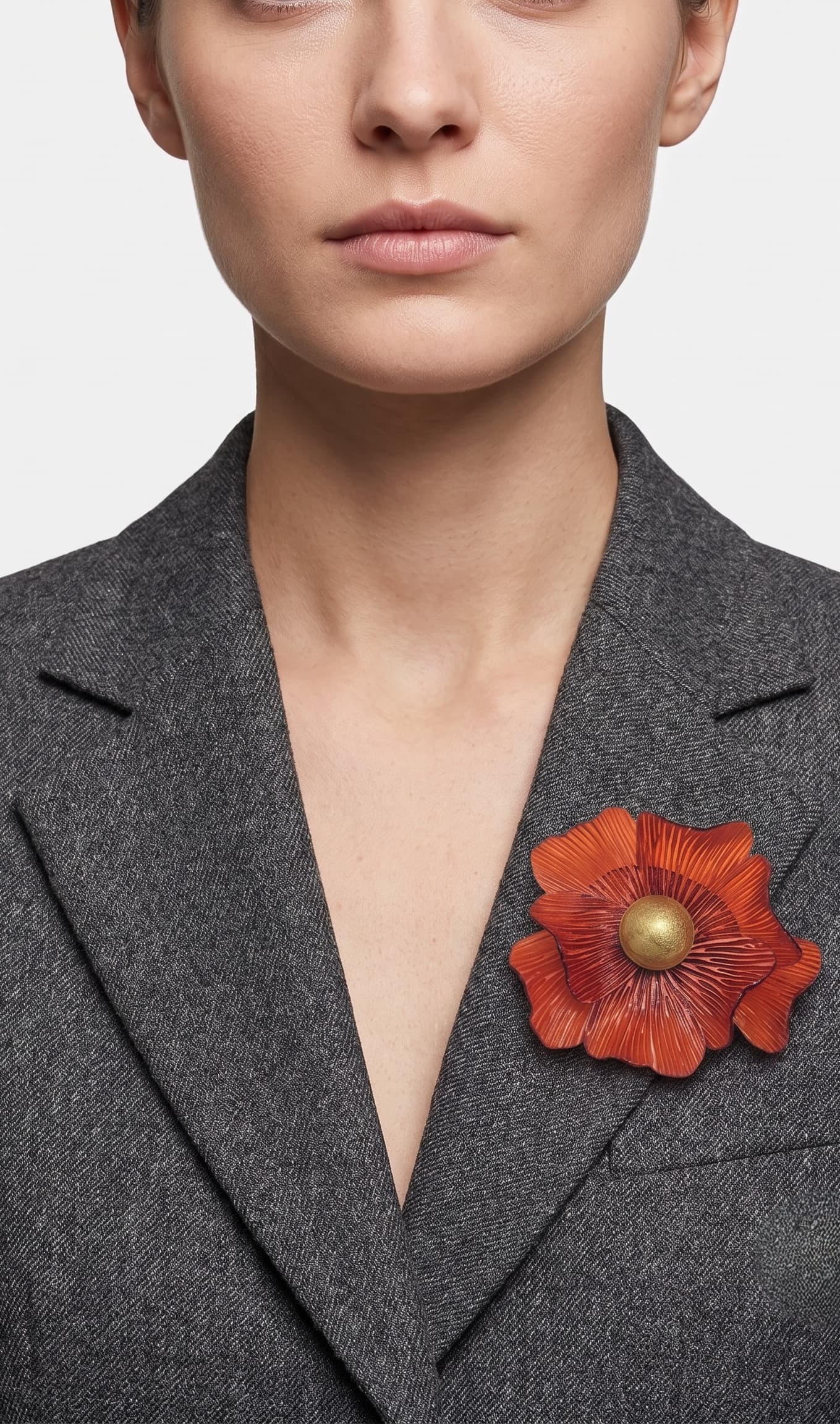 modelo de frente portando el broche maxi de anémona naranja prendido en la solapa de una americana de sastre gris oscuro, apreciando su escala y relieve.
