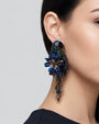 modelo luciendo el pendiente Perroquet Bleu en la oreja, apreciando su silueta de ave, volumen floral y escala sobre la piel.
