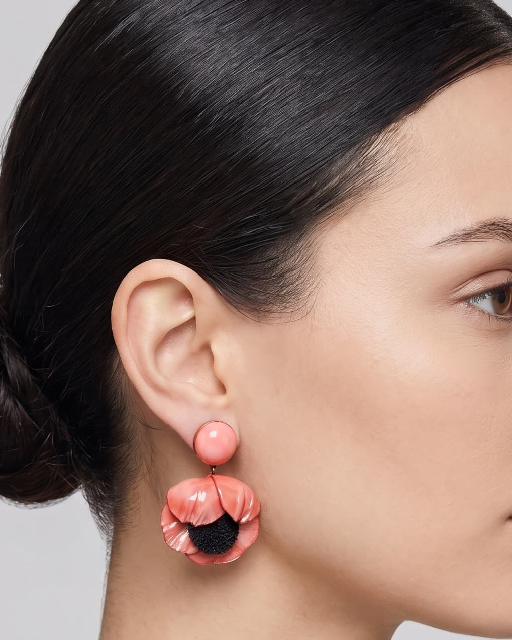 modelo luciendo el pendiente colgante de amapola rosa, apreciando su escala maximalista, su relieve tridimensional y cómo adorna el rostro con sofisticación.