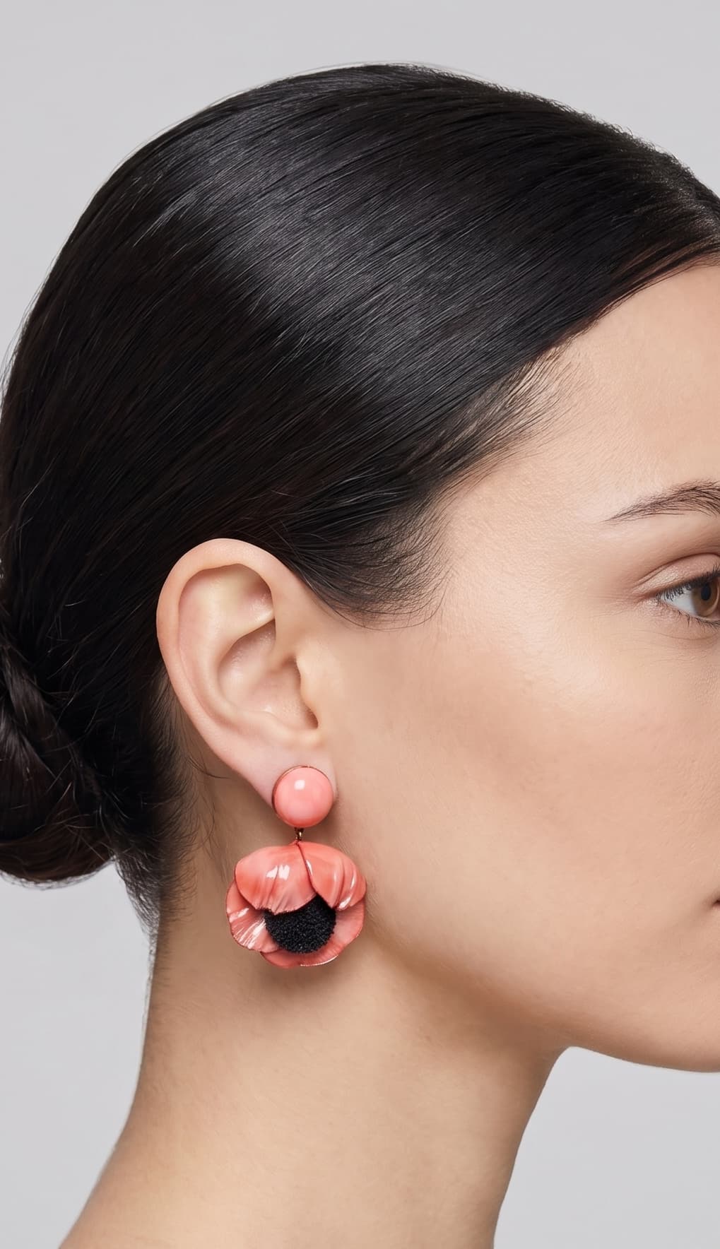 modelo luciendo el pendiente colgante de amapola rosa, apreciando su escala maximalista, su relieve tridimensional y cómo adorna el rostro con sofisticación.