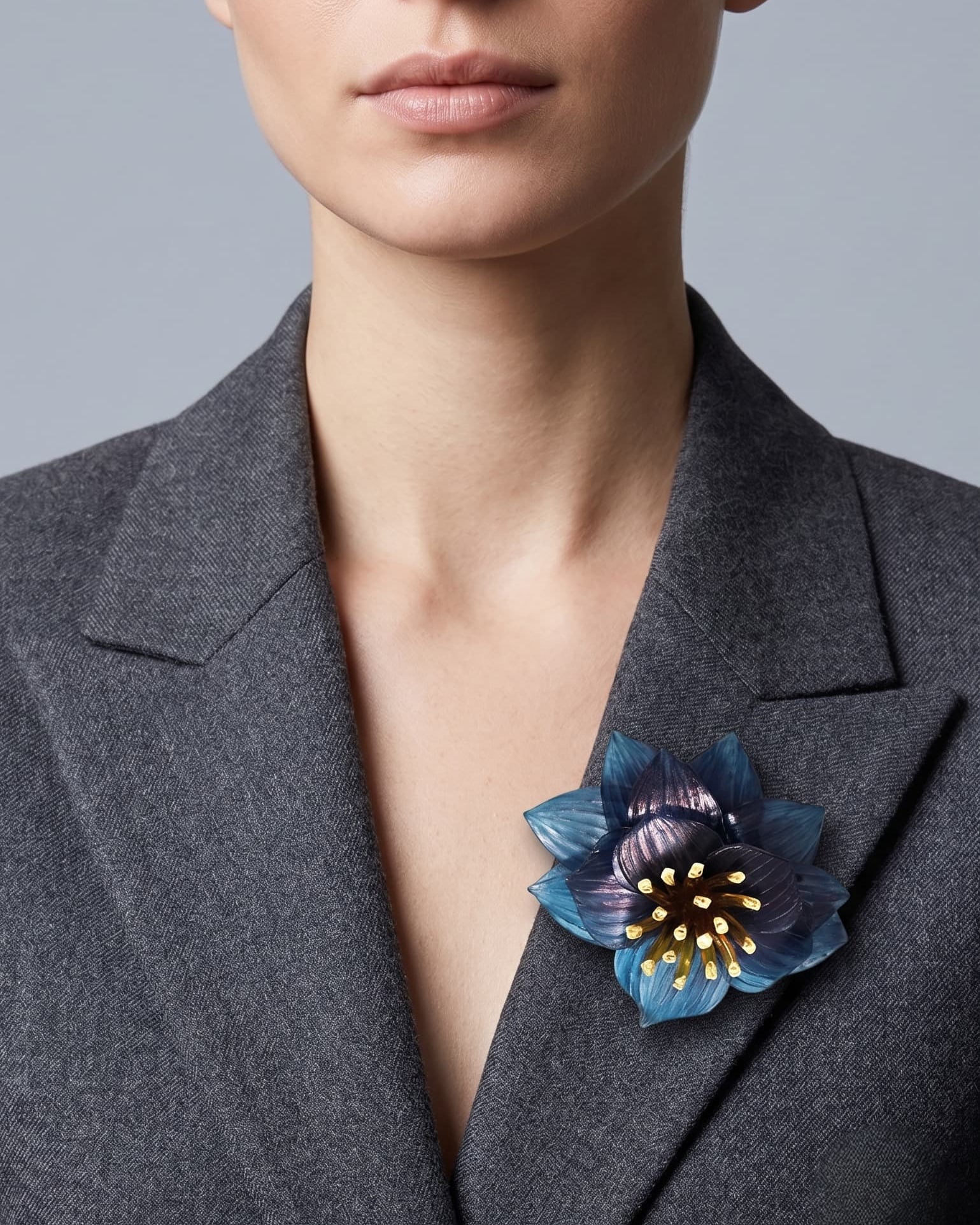 modelo de frente luciendo el broche maxi de loto azul prendido en la solapa de una americana de sastre gris oscuro, mostrando su escala sofisticada y elegante.