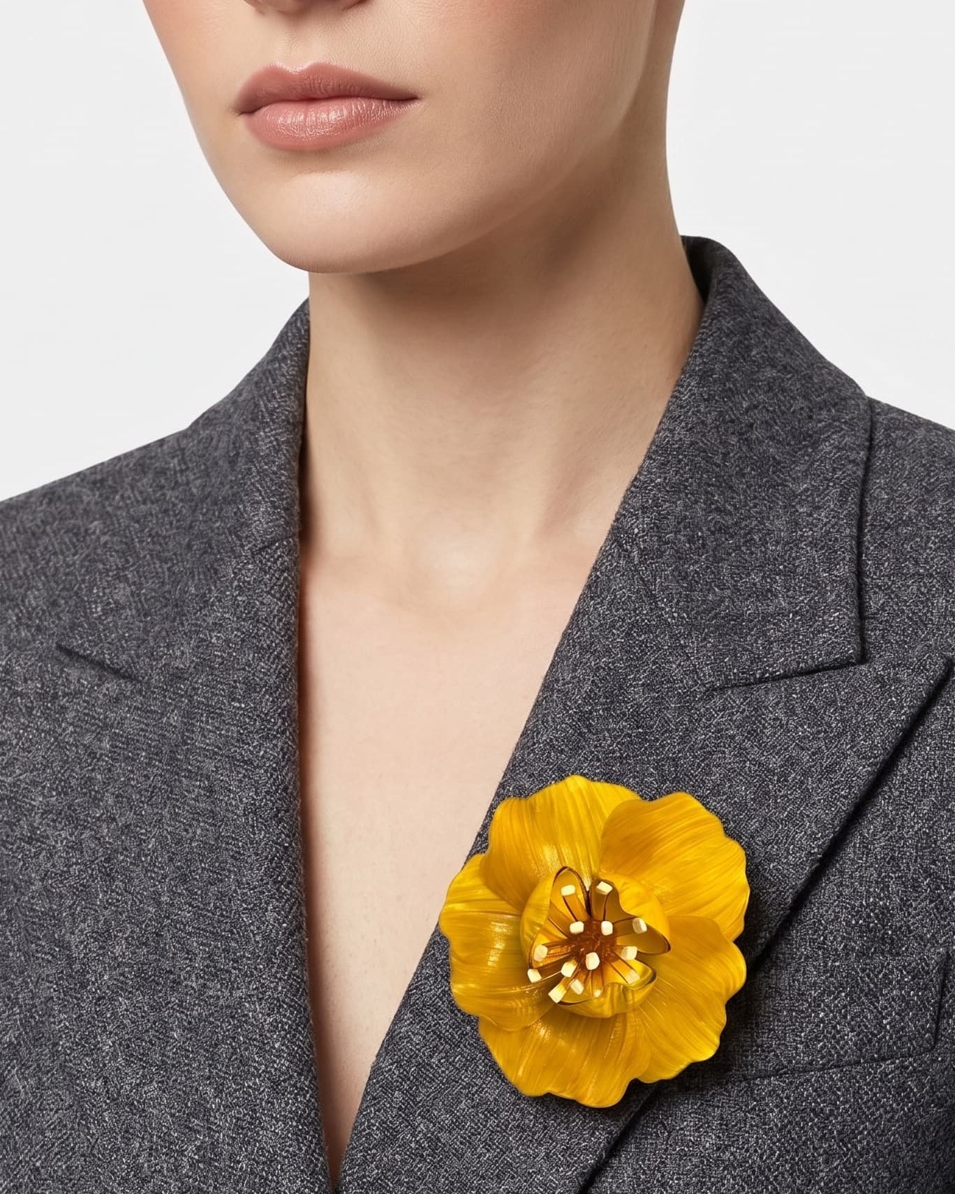 vista frontal del broche de flor de Ciléa Paris colocado en la solapa de una chaqueta de sastre gris, detallando su escala maxi y su elegancia luminosa.