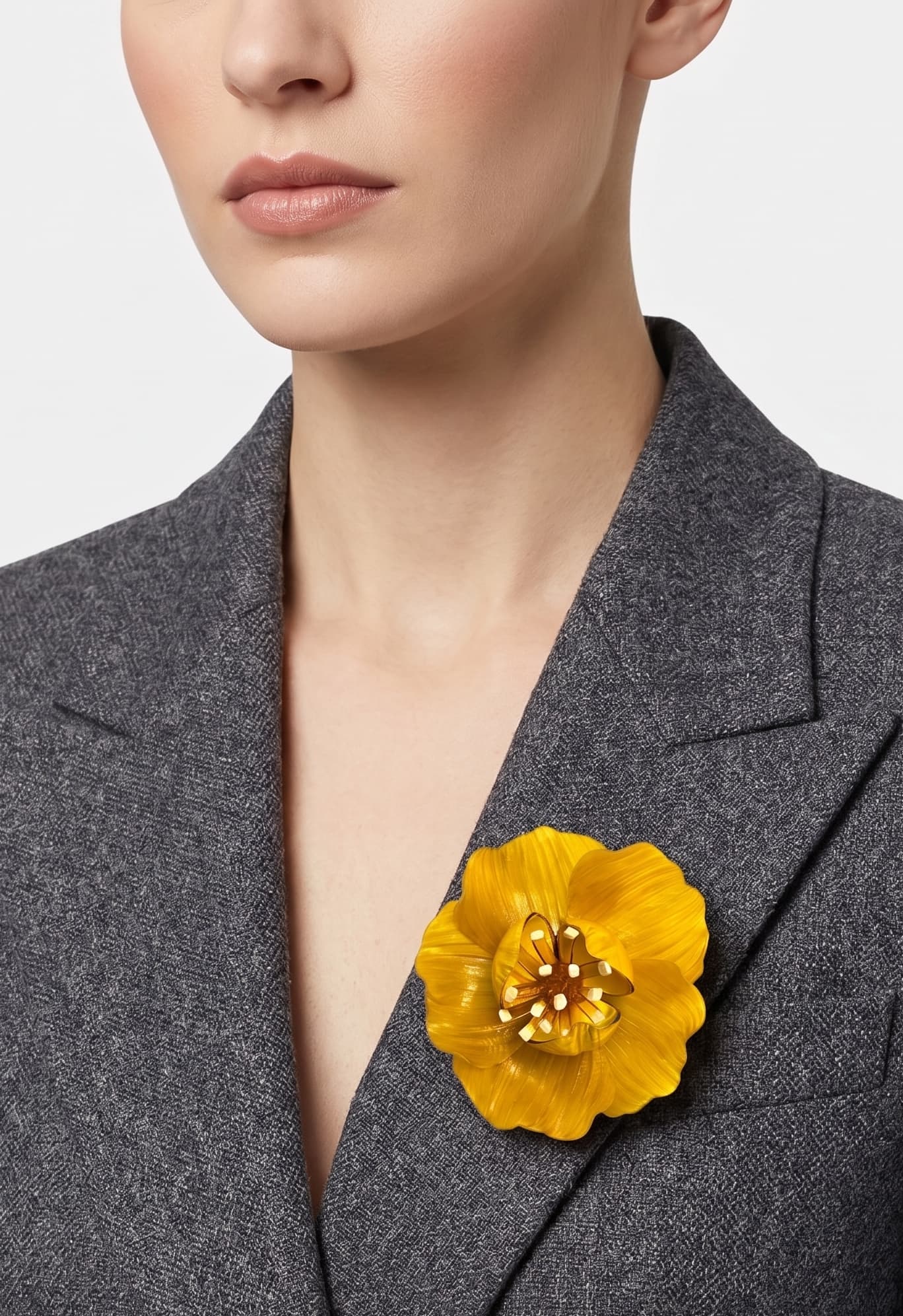 vista frontal del broche de flor de Ciléa Paris colocado en la solapa de una chaqueta de sastre gris, detallando su escala maxi y su elegancia luminosa.