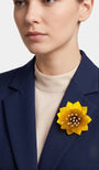 modelo de frente portando el broche maxi de loto amarillo prendido en la solapa de una blazer de sastre azul marino, destacando su escala sofisticada y su gran luminosidad.